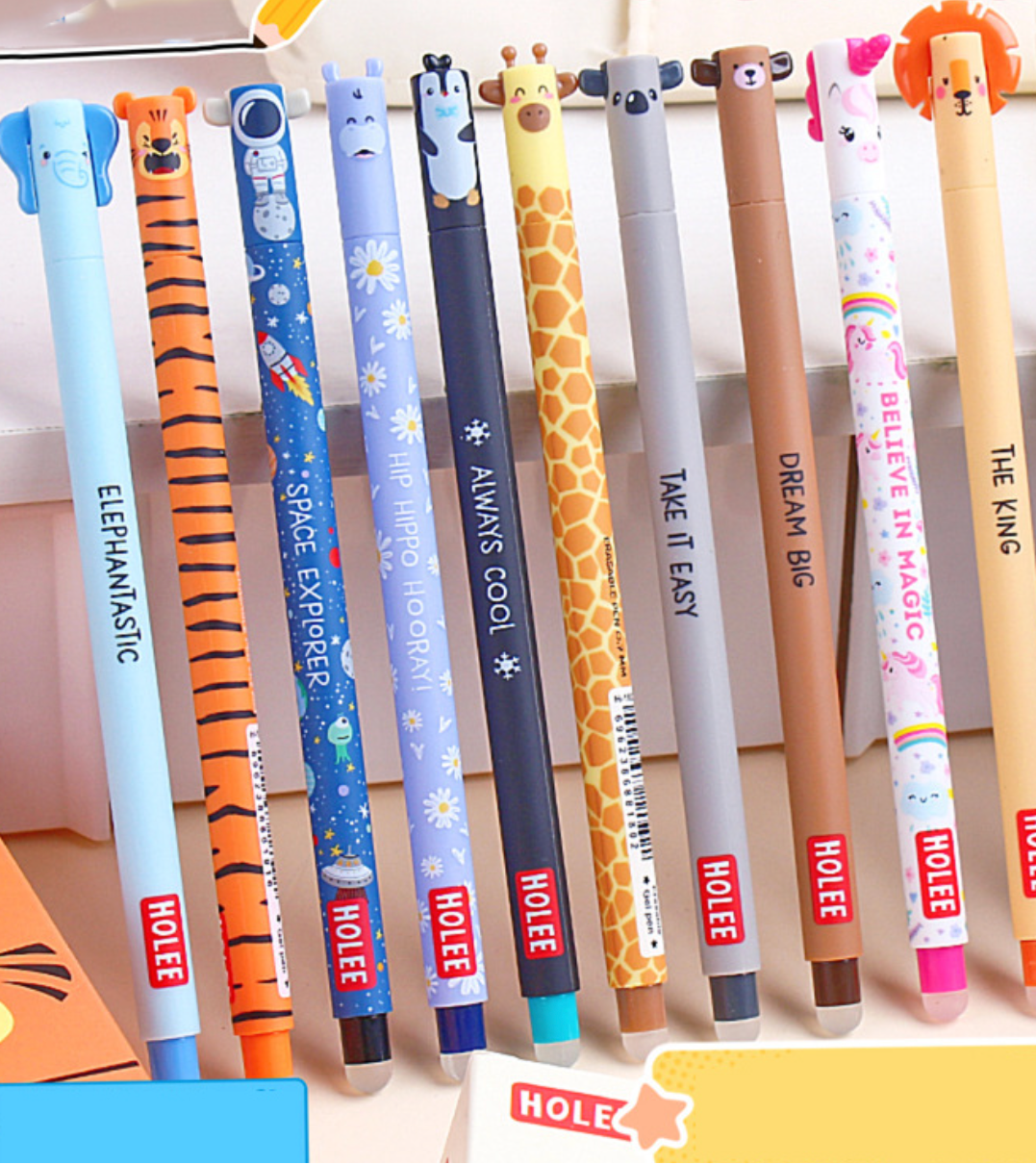 A set of nine cartoon-themed hole-in-one pencils standing upright in a row. The pencils feature animal and space designs including an elephant, tiger, rocket ship, space explorer, giraffe, panda, bear, unicorn, and a lion.